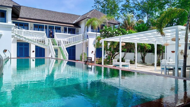 A swimming pool with a white pergola and lounge chairs, a staircase leading to a blue door, and a white building with blue shutters in the background. - The Trawangan Resort (Gili Trawangan)