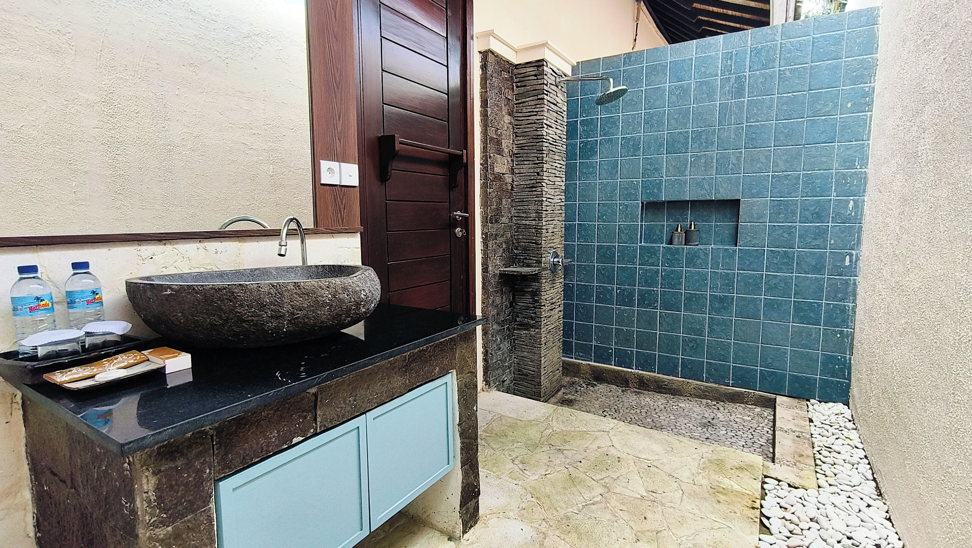 Een badkamer met een stenen wastafel, een douche met blauwe tegels en een houten deur.