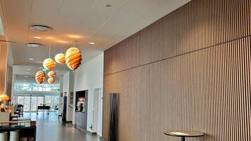 A modern hotel lobby with a long corridor, wooden panel wall, and hanging spherical light fixtures.
