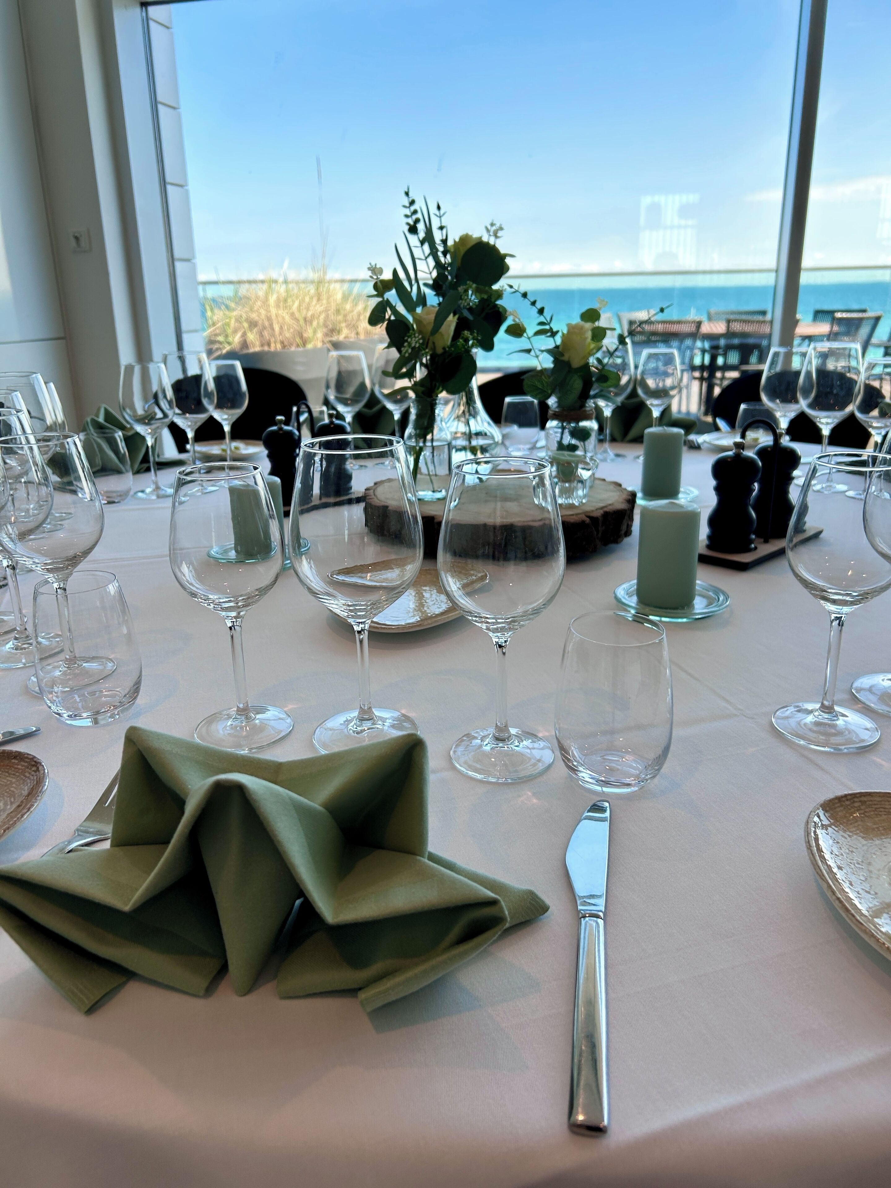 Una mesa lista para cenar, con copas de vino, una vela y vistas al océano.