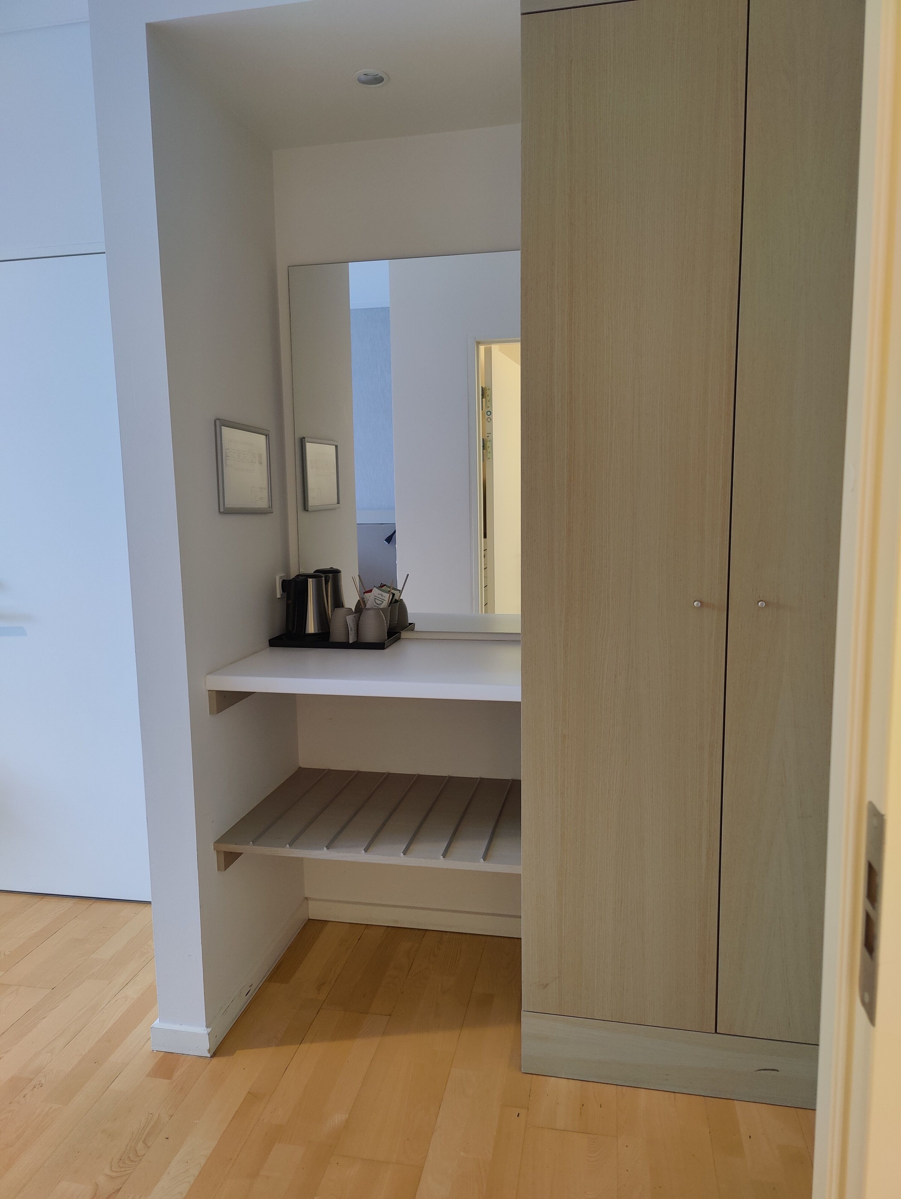 Een kamer met een houten garderobe, een witte plank met keukenbenodigdheden en een houten vloer.