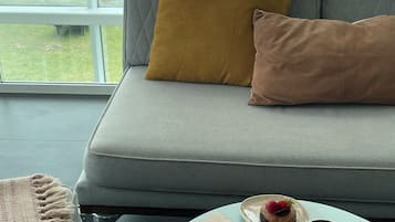 Una habitación con sofá, una mesa con postre, tazas de café y vista al mar.