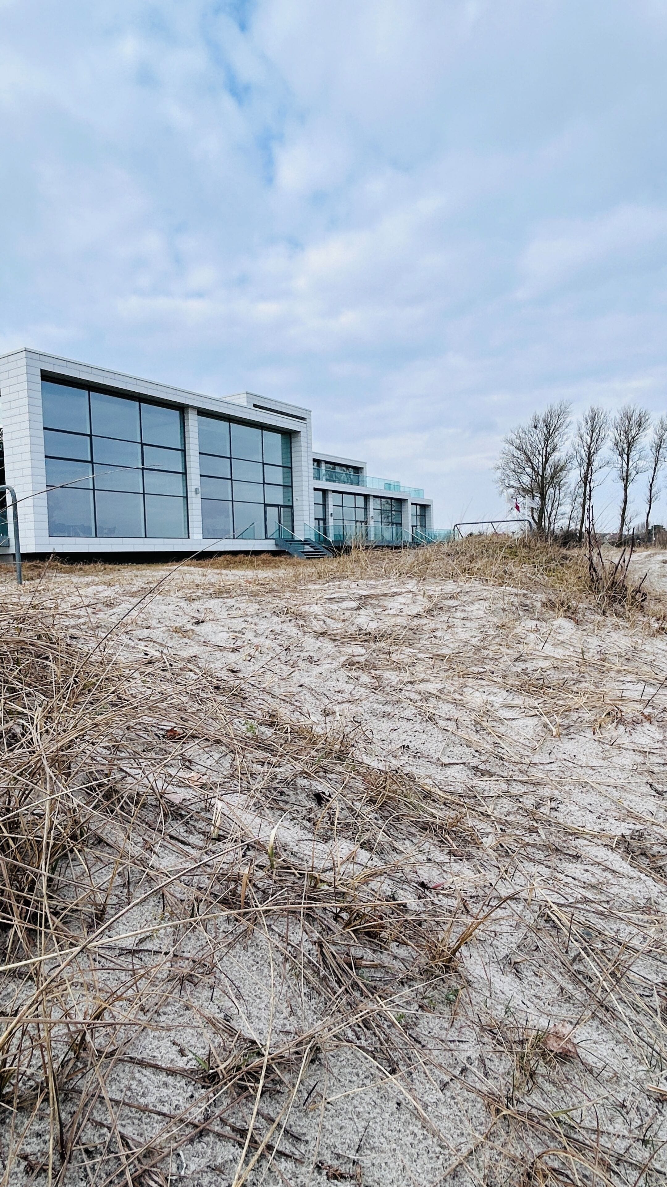 A modern building with large windows and a flat roof, surrounded by dry grass and a clear sky.