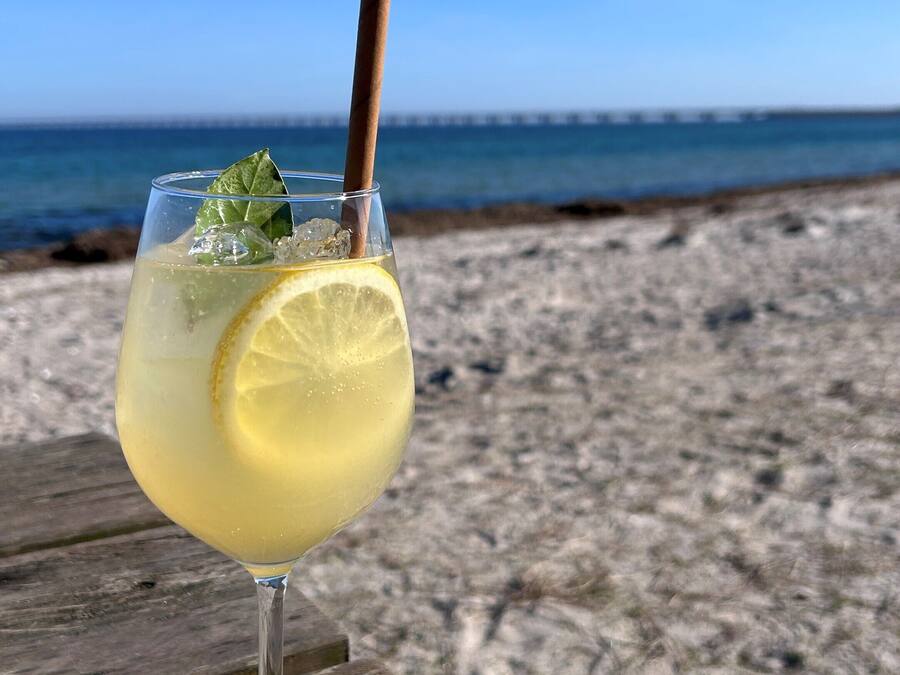 A glass of a light-colored beverage with a straw and a lemon slice on a wooden surface.