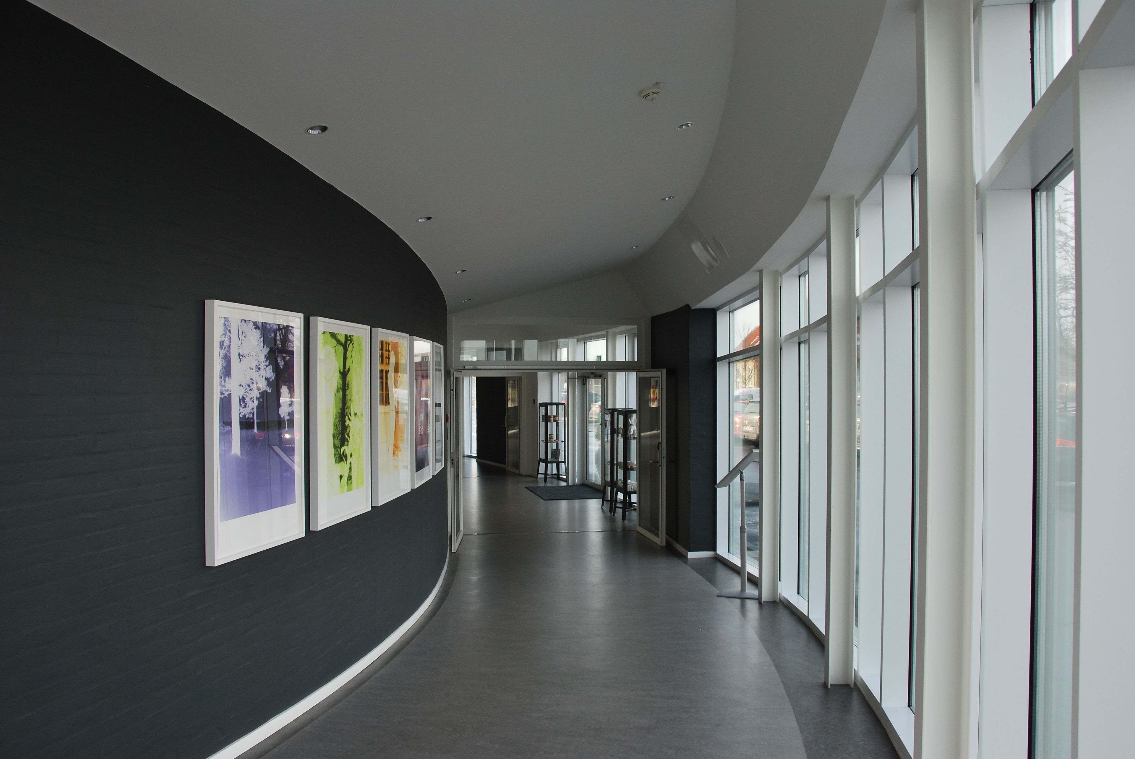 A modern hallway with a curved wall, large windows, and framed artwork.