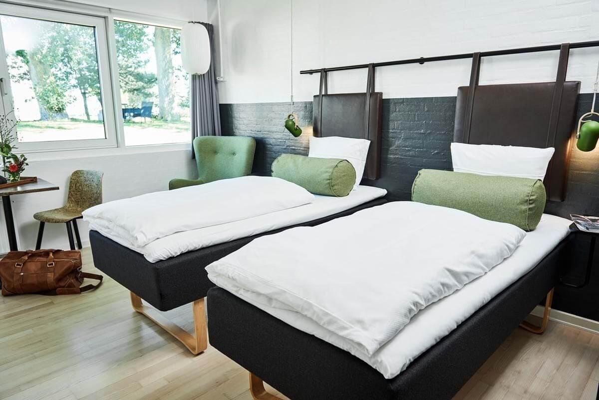 A modern hotel room with two single beds, a desk, and a chair.