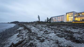 Un edificio moderno con grandes ventanales, una valla de madera y una playa al fondo.