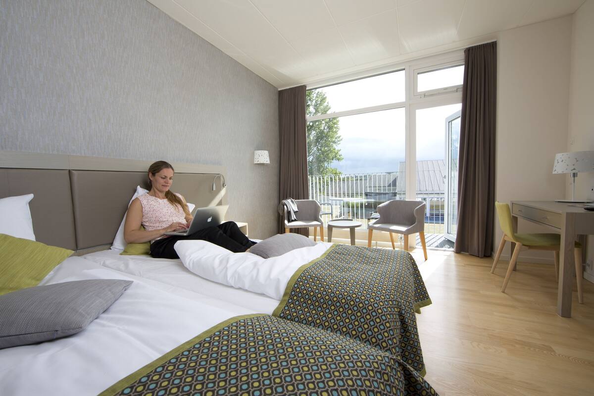 A hotel room with a bed, a desk, and a balcony with chairs.