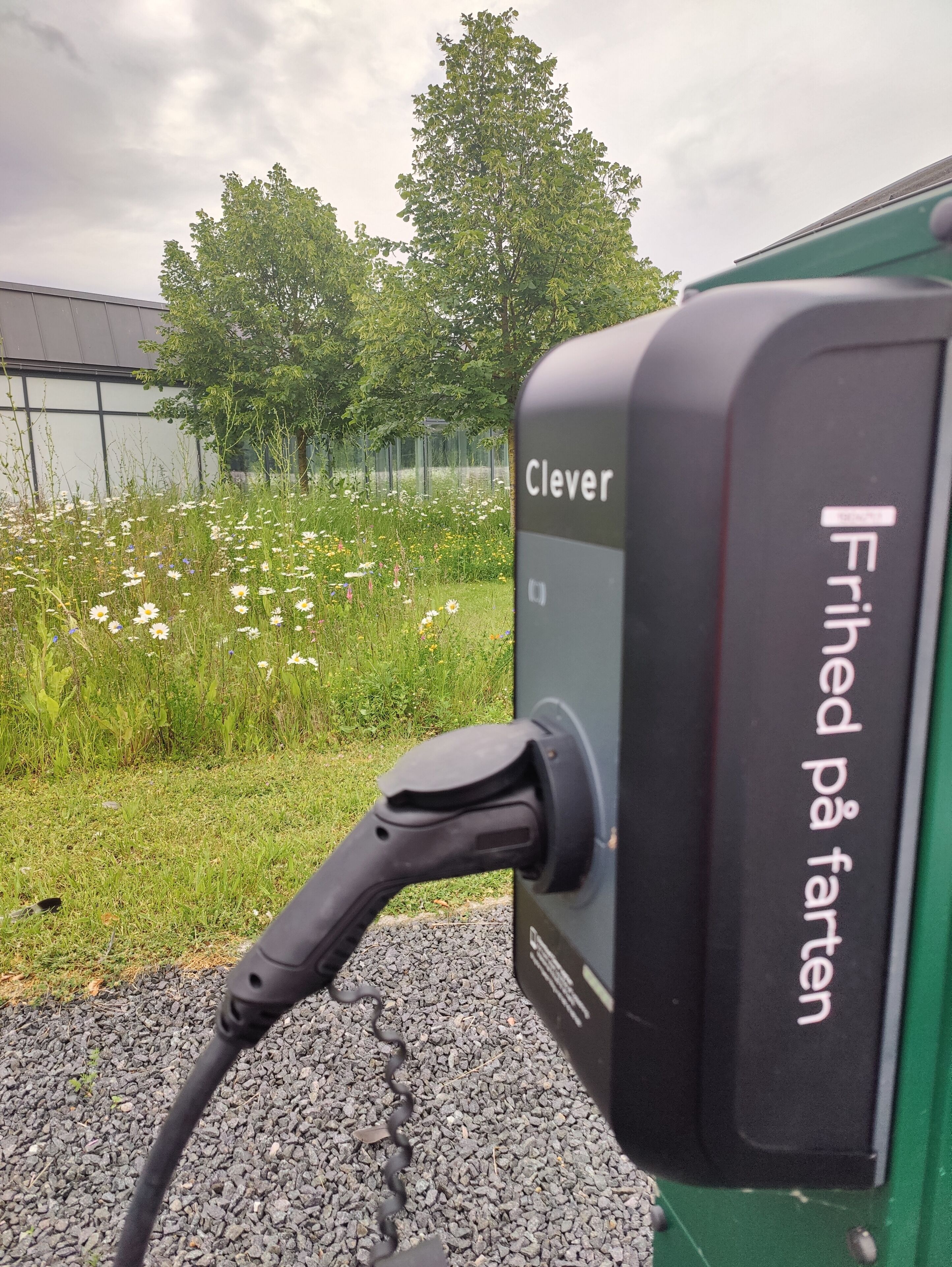 Une borne de recharge pour véhicules électriques portant les mentions « Clever » et « Frihed på faetten », indiquant une zone de stationnement gratuite.