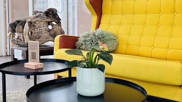 A yellow sofa, a potted plant, a skull display, and a black table in a room with a carpeted floor.