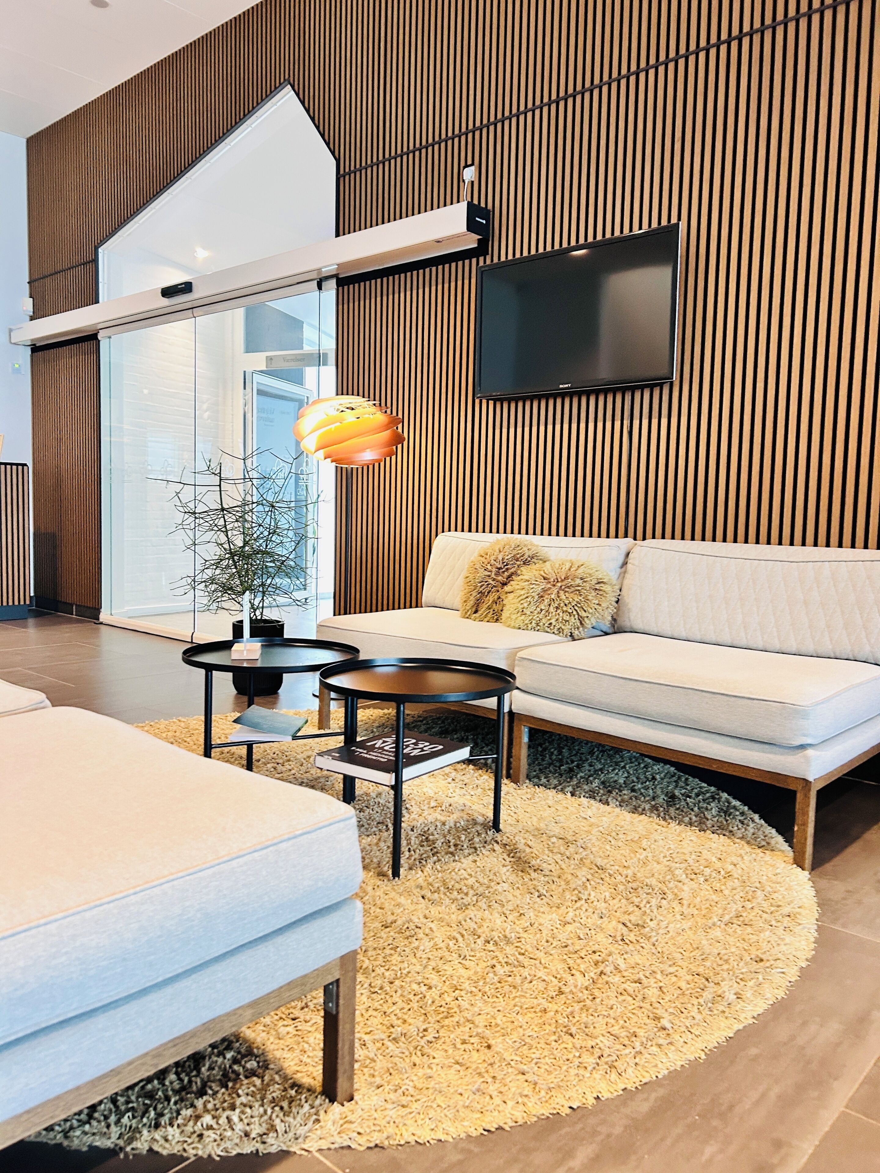 A modern living room with a sofa, a coffee table, a floor lamp, and a television mounted on a wooden wall.