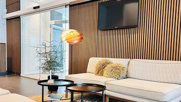 A modern living room with a sofa, a coffee table, a floor lamp, and a television mounted on a wooden wall.