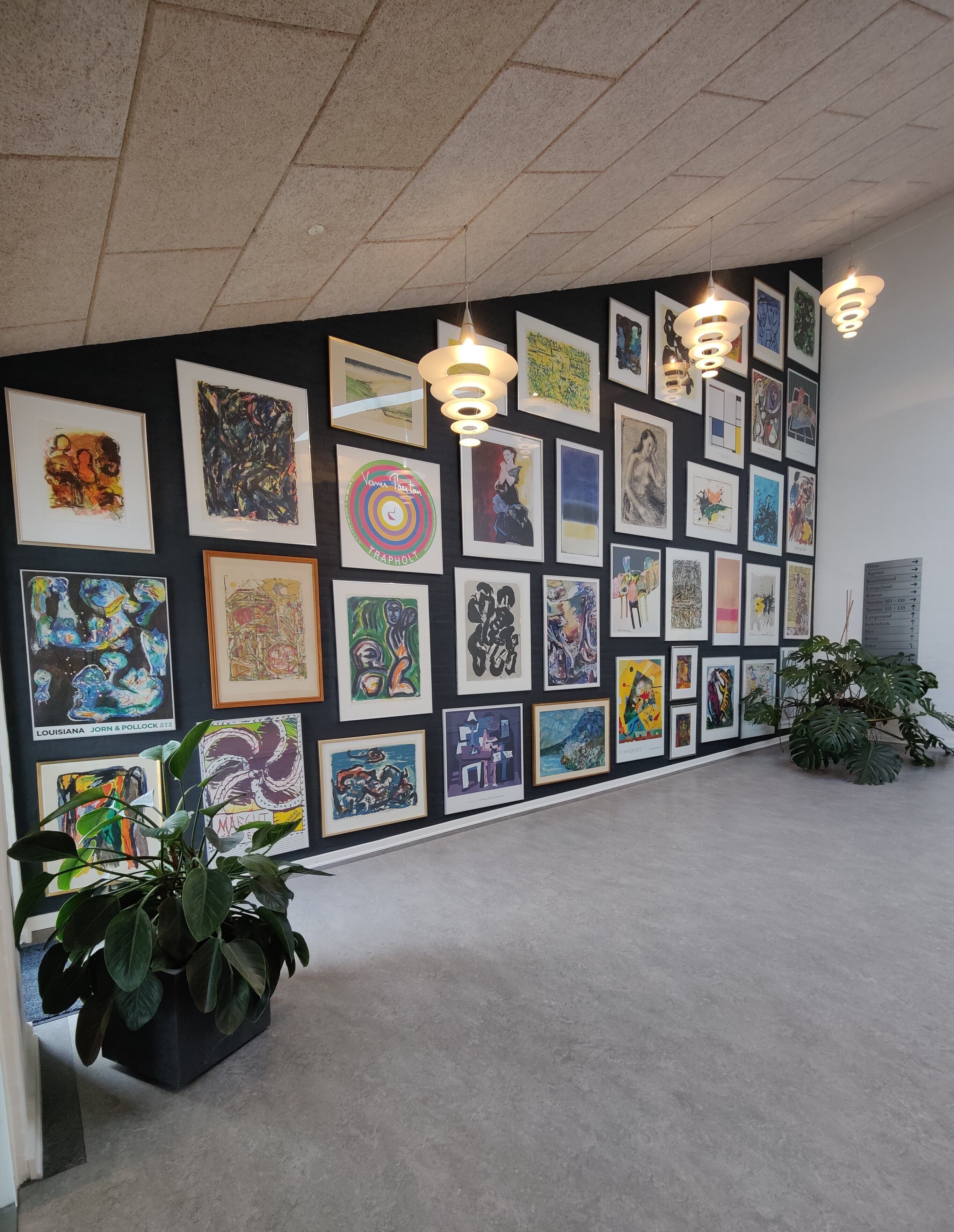 Een galerijwand met diverse ingelijste kunstwerken, een kamerplant en hanglampen.