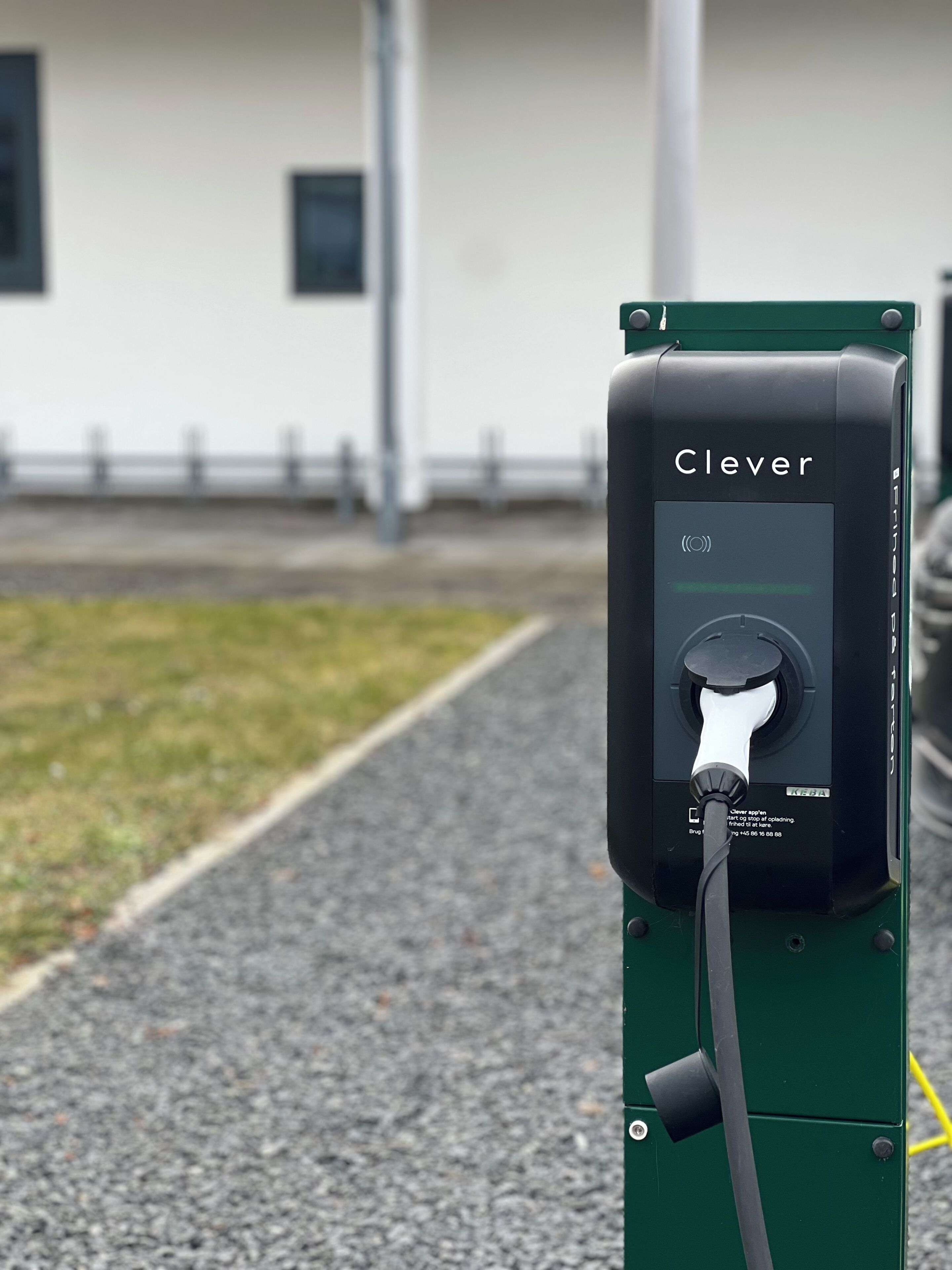 A Clever electric vehicle charging station with a green base, a charging plug, and a control panel with a power button and instructions.