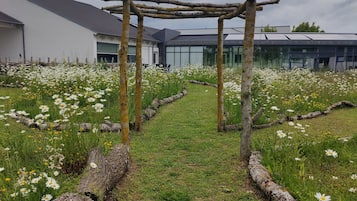 A pathway leading to a wooden pergola in a garden with white flowers and logs.