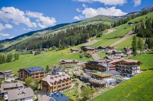 Un complejo turístico de montaña con varias construcciones de estilo chalet, pistas de esquí y un cielo azul despejado.