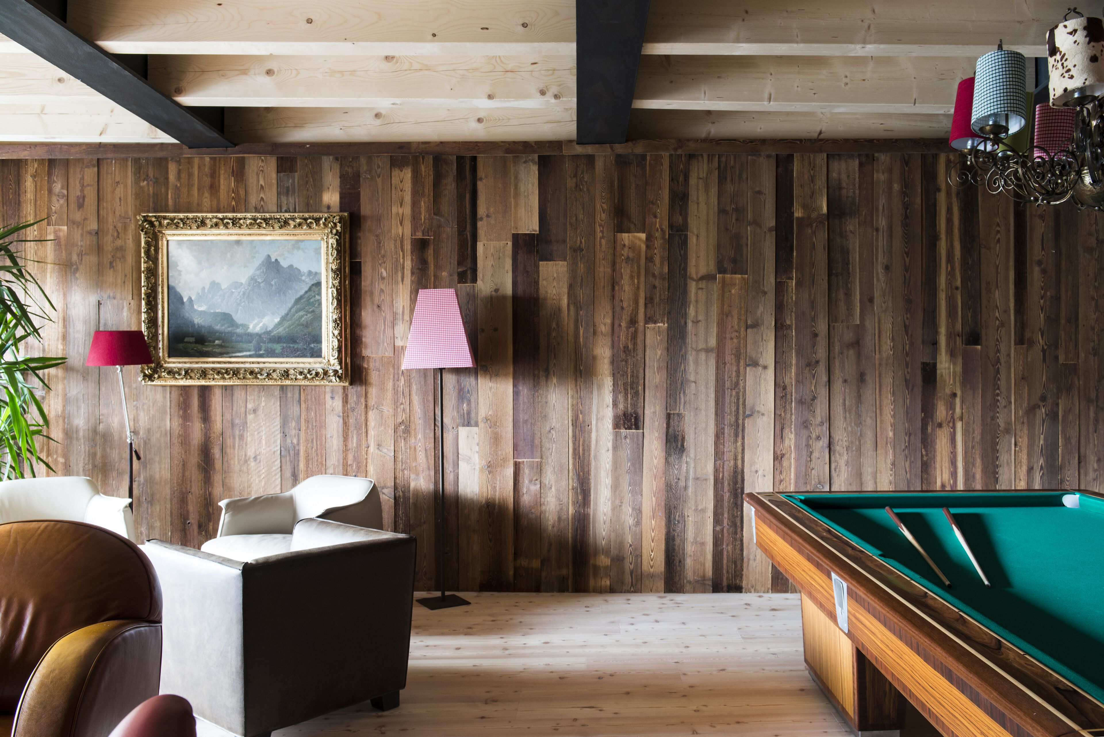 A wooden-paneled room with a pool table, a framed painting, and a lamp.