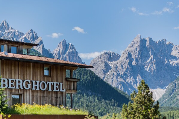 A wooden building with a sign reading "BERGHOTEL" and a mountainous backdrop. - Berghotel (Sesto)