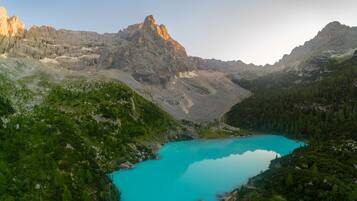 Paisaje montañoso con un lago turquesa rodeado de bosques densos y cumbres rocosas.