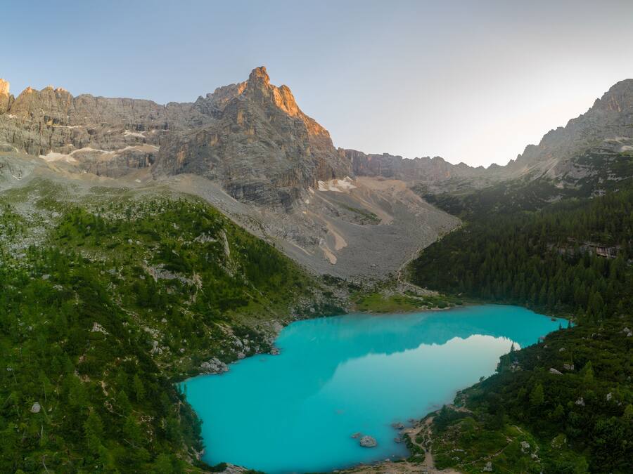 Paisaje montañoso con un lago turquesa rodeado de bosques densos y cumbres rocosas.