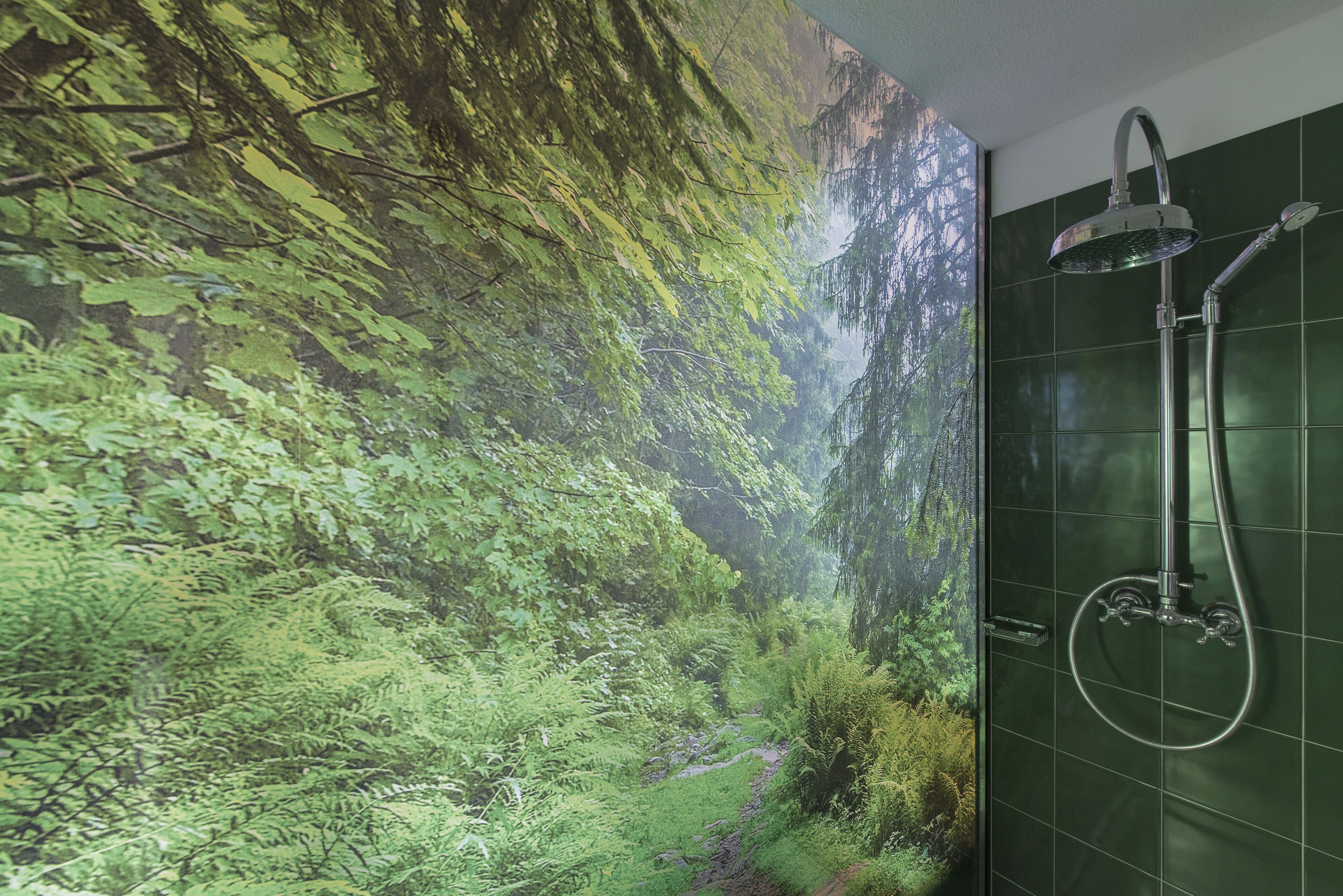 Un baño con pared de azulejos verdes y una ducha.
