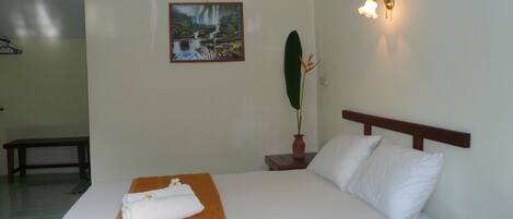 Habitación de hotel con una cama, una mesita de noche con un florero y un cuadro de una cascada, además de una lámpara fijada en la pared.