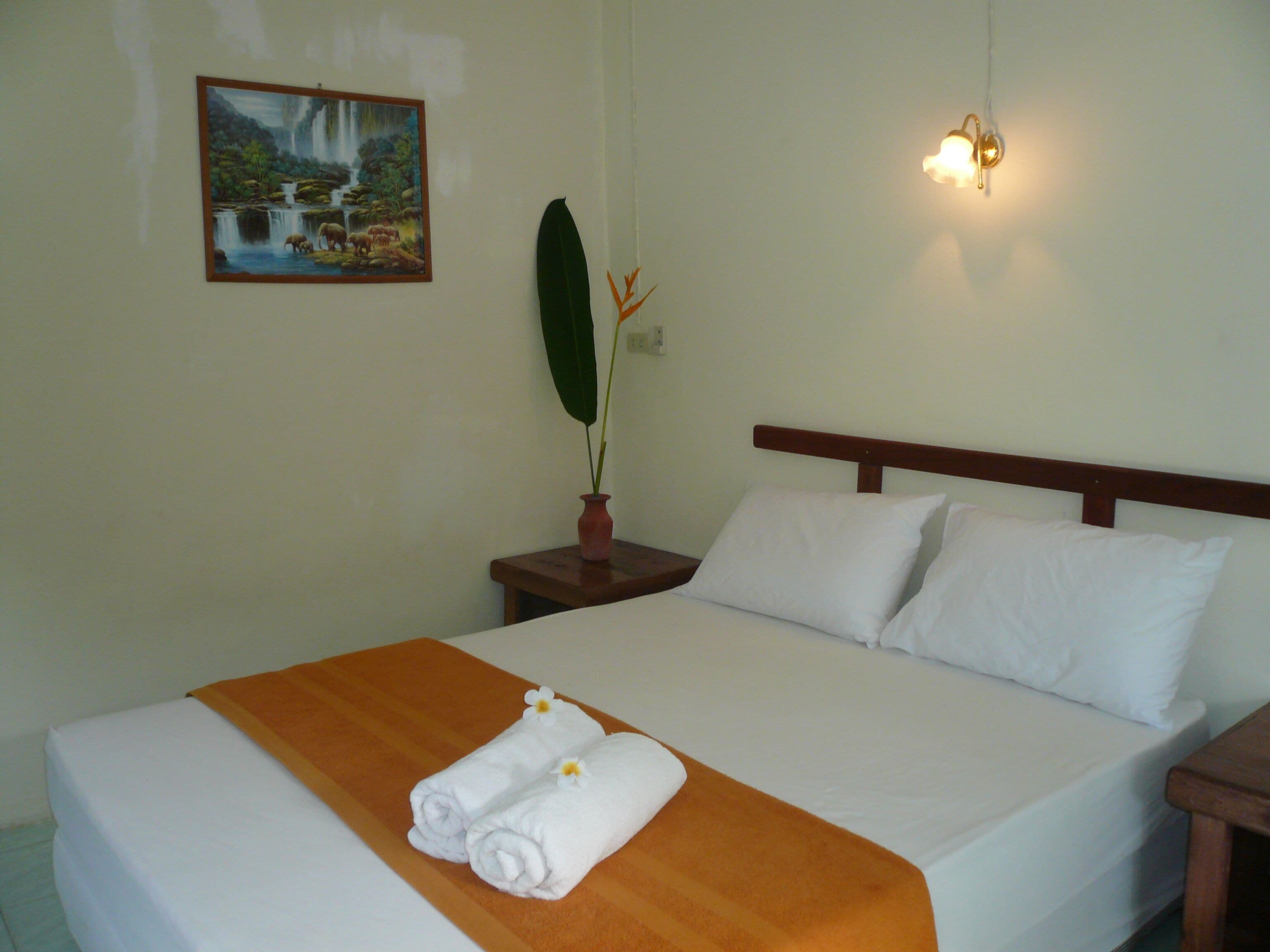 Habitación de hotel con una cama, un cuadro de una cascada, una mesita de noche con una planta y una lámpara de pared.