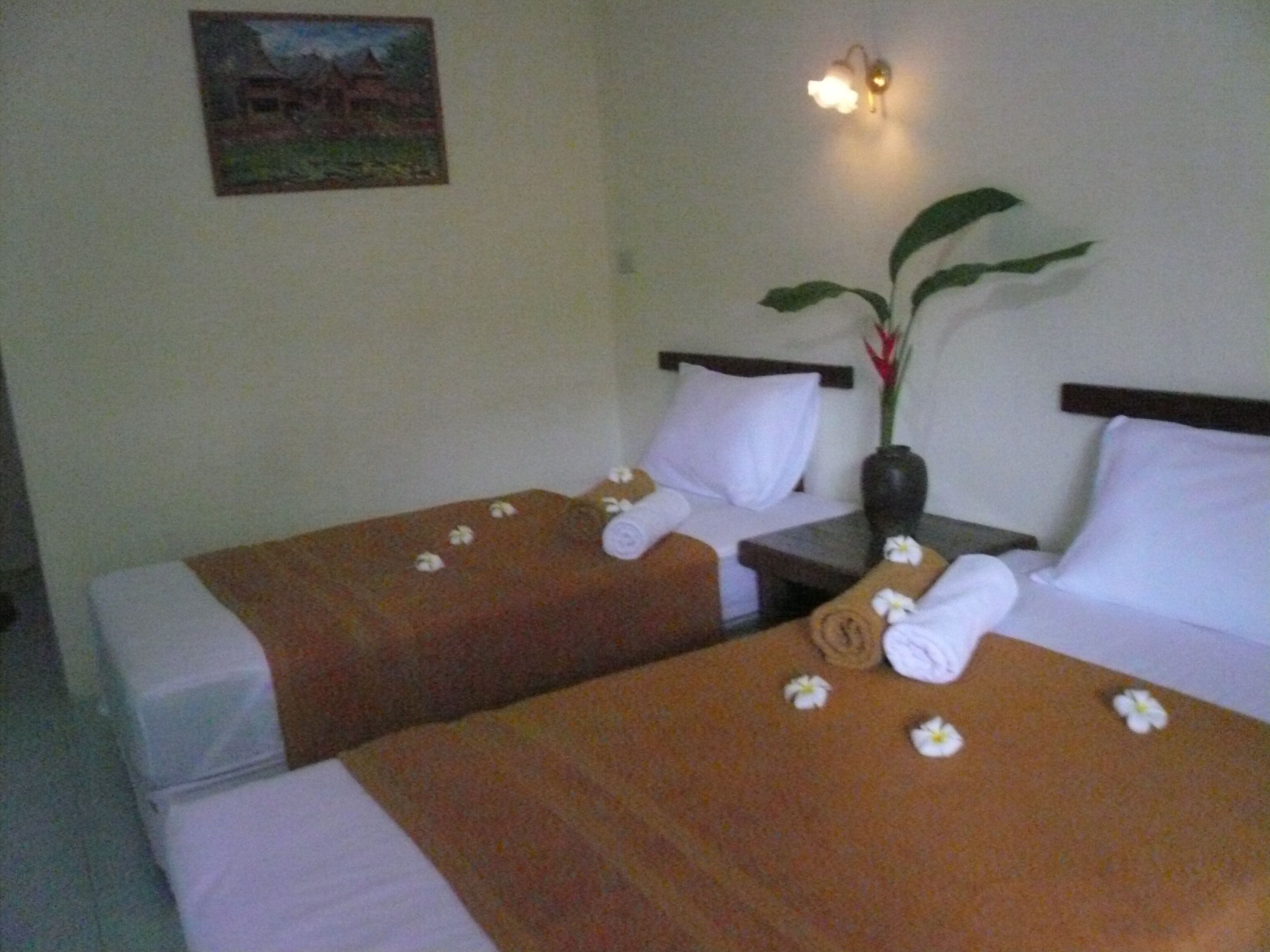A hotel room with two beds, each with white linens and brown headboards. There is a painting on the wall and a vase with a plant on the nightstand.