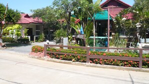 A resort with a red-roofed building, a signboard, and a paved walkway with flower beds.