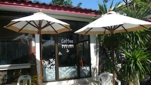 A coffee shop with outdoor seating, white plastic chairs, and umbrellas.
