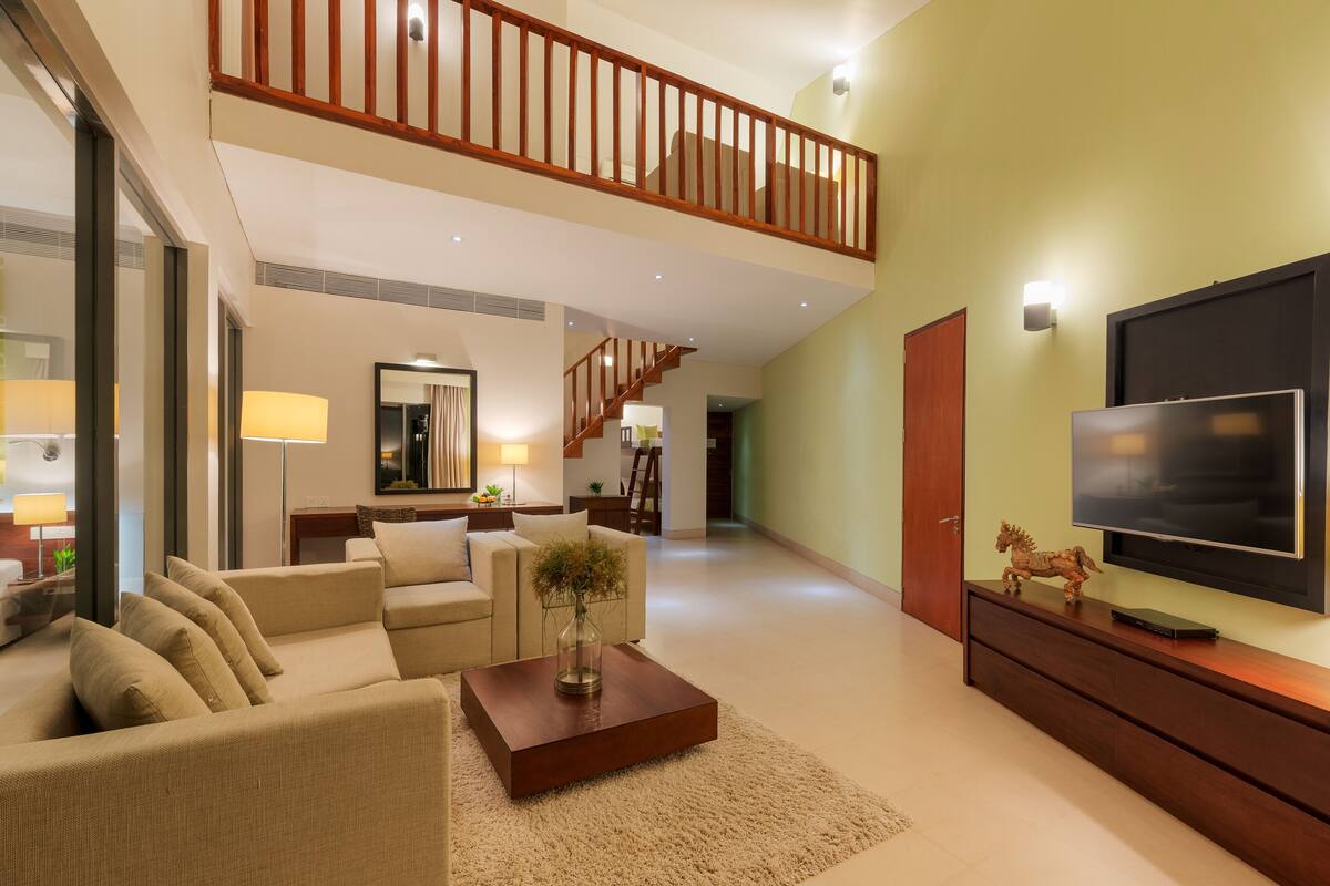 A spacious living room with a high ceiling, a staircase, a flat-screen TV, and a cozy seating area.