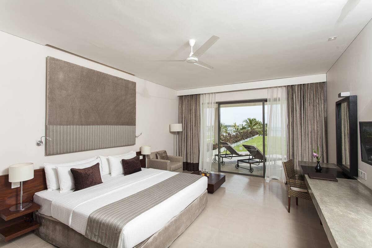 A modern hotel room with a large bed, a desk, and a balcony with a view.