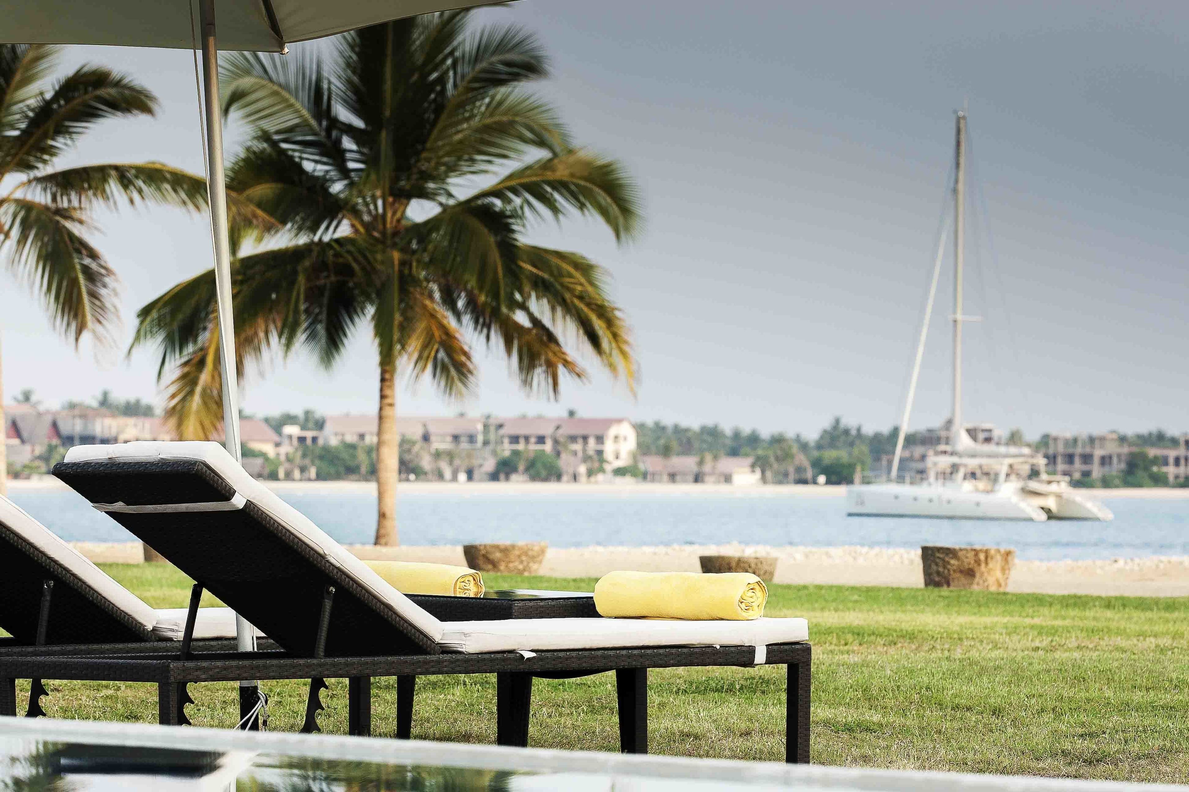 A poolside area with lounge chairs and a view of a yacht and buildings in the background.