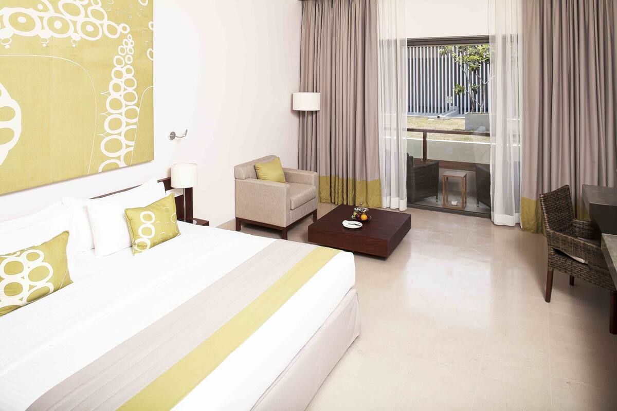 A hotel room with a large bed, a sofa, a coffee table, and a dining area with a table and chairs.
