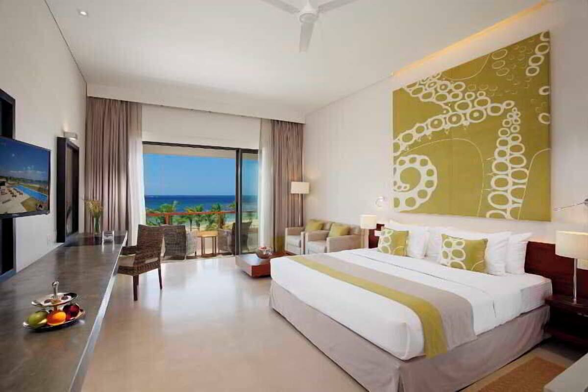 A hotel room with a large bed, a dining area, and a view of the ocean.