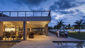 Un hotel moderno con un comedor al aire libre cubierto, piscina y vistas al mar.
