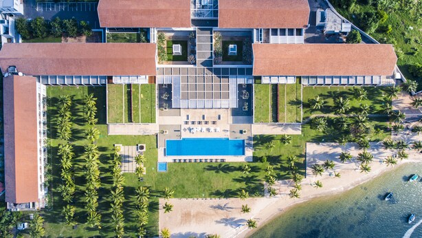 Vista aérea de un resort con una gran piscina, palmeras y una playa.