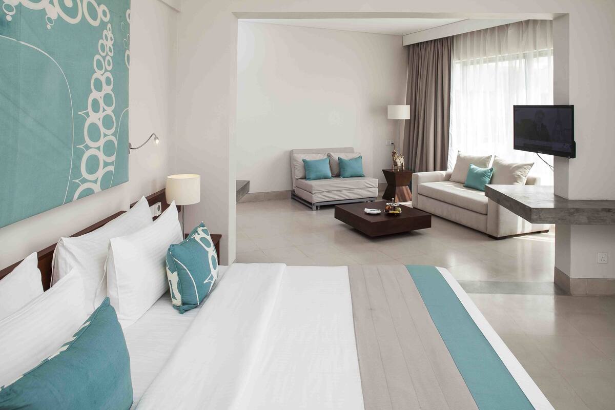 A modern hotel room with a large bed, two sofas, a coffee table, and a TV.