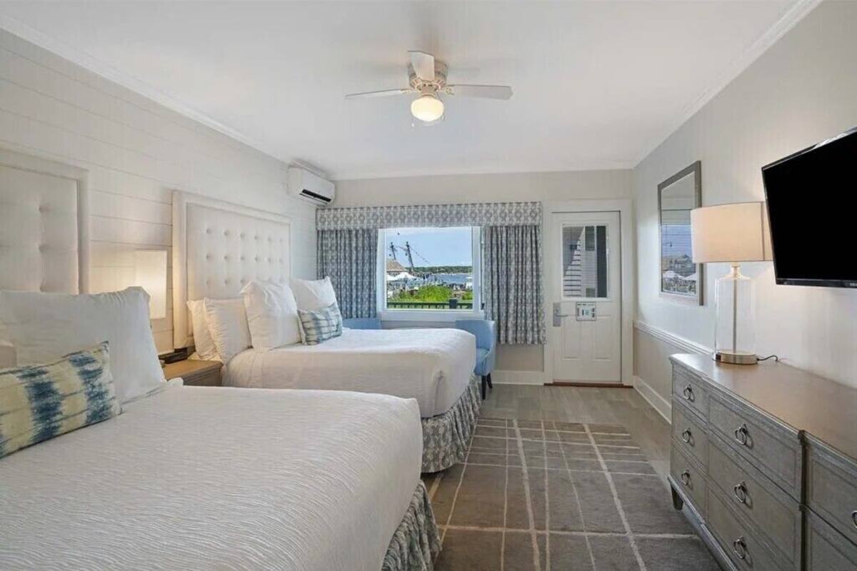 Habitación de hotel con dos camas, ventilador de techo, televisión, cómoda y ventana con cortinas.