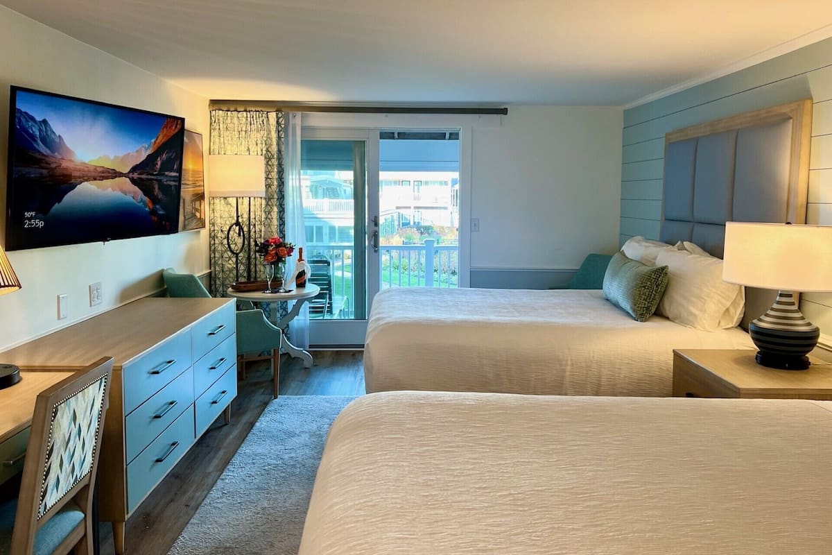 Habitación de hotel con dos camas, un escritorio, un televisor y un balcón con vistas.