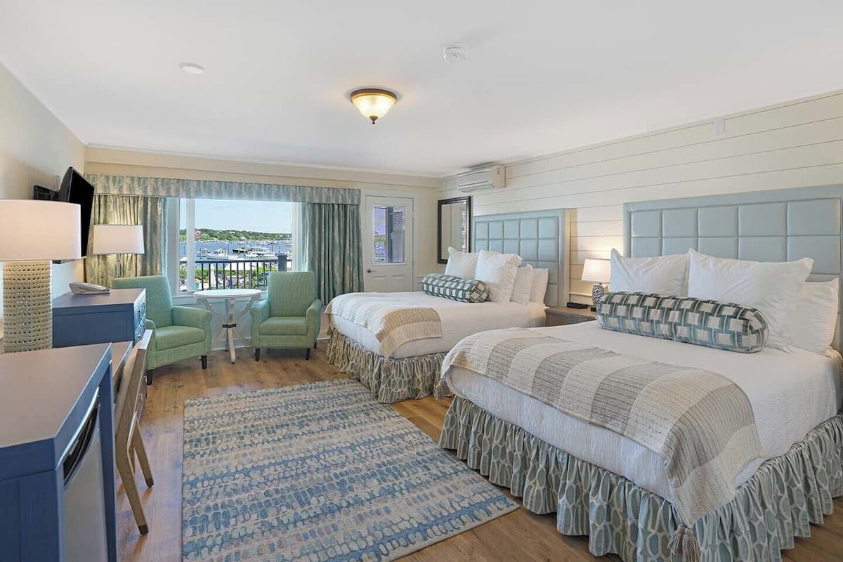 Habitación de hotel con dos camas, un escritorio, una silla, vista al mar y un balcón.