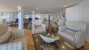 A spacious living room with striped armchairs, a wooden coffee table with a decorative bowl, and a view of the adjacent dining area. - The Harborside Inn (Edgartown)