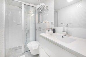 Un baño moderno con ducha acristalada, lavamanos blanco y un espejo grande.