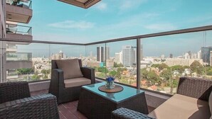 A balcony with wicker furniture and a glass table, overlooking a cityscape. - Tel Aviv Home (Tel Aviv)