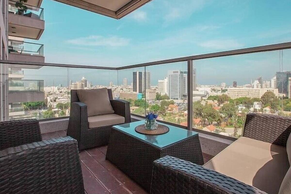 Un balcón con mobiliario de mimbre y una mesa de vidrio, con vistas a un paisaje urbano.