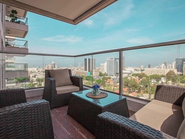 Un balcón con mobiliario de mimbre y una mesa de vidrio, con vistas a un paisaje urbano.
