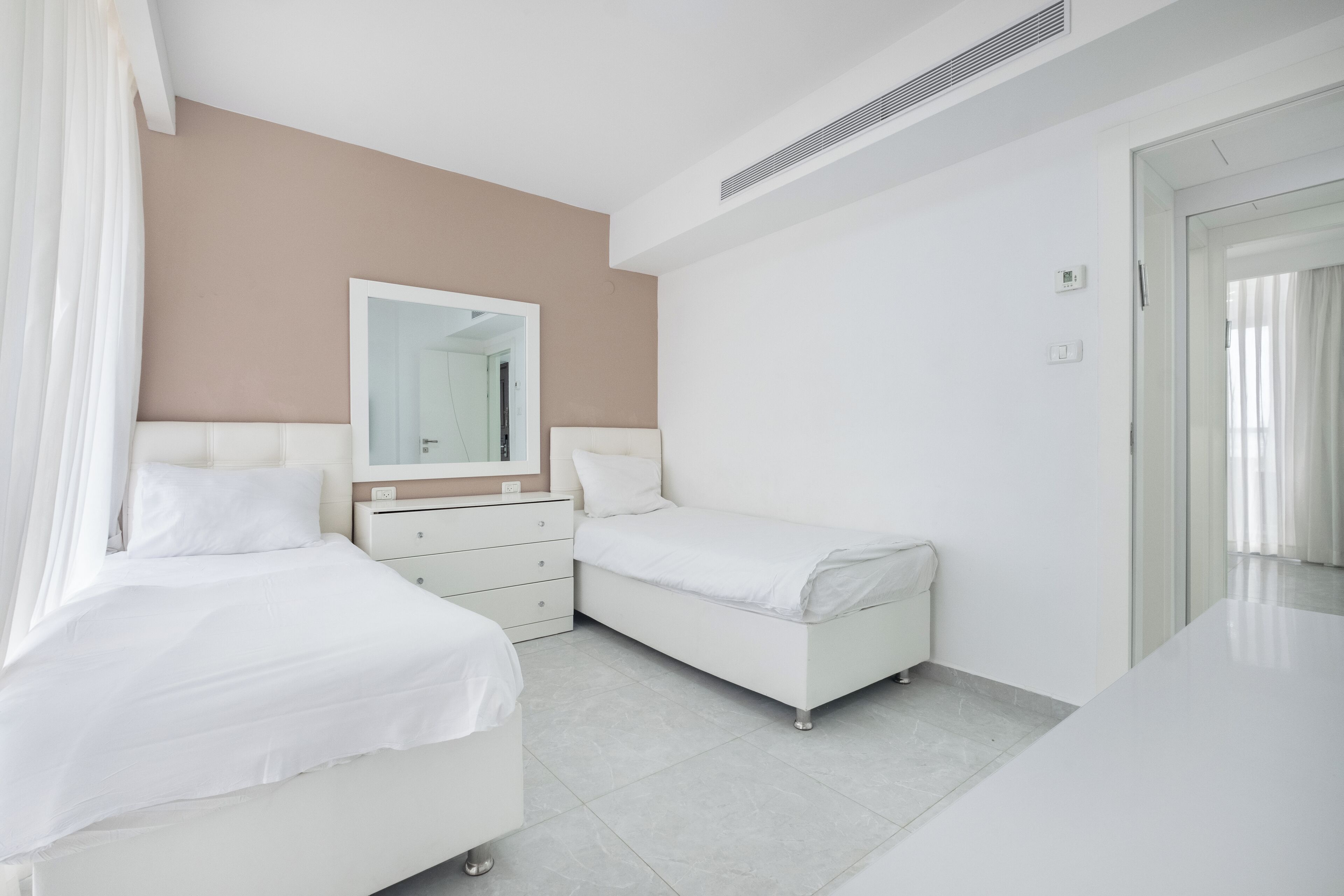 A modern hotel room with two beds, a large mirror, a white dresser, and a bathroom visible through an open door.