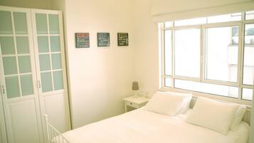 A bedroom with a bed, a nightstand, a lamp, and a window. There are three posters on the wall.