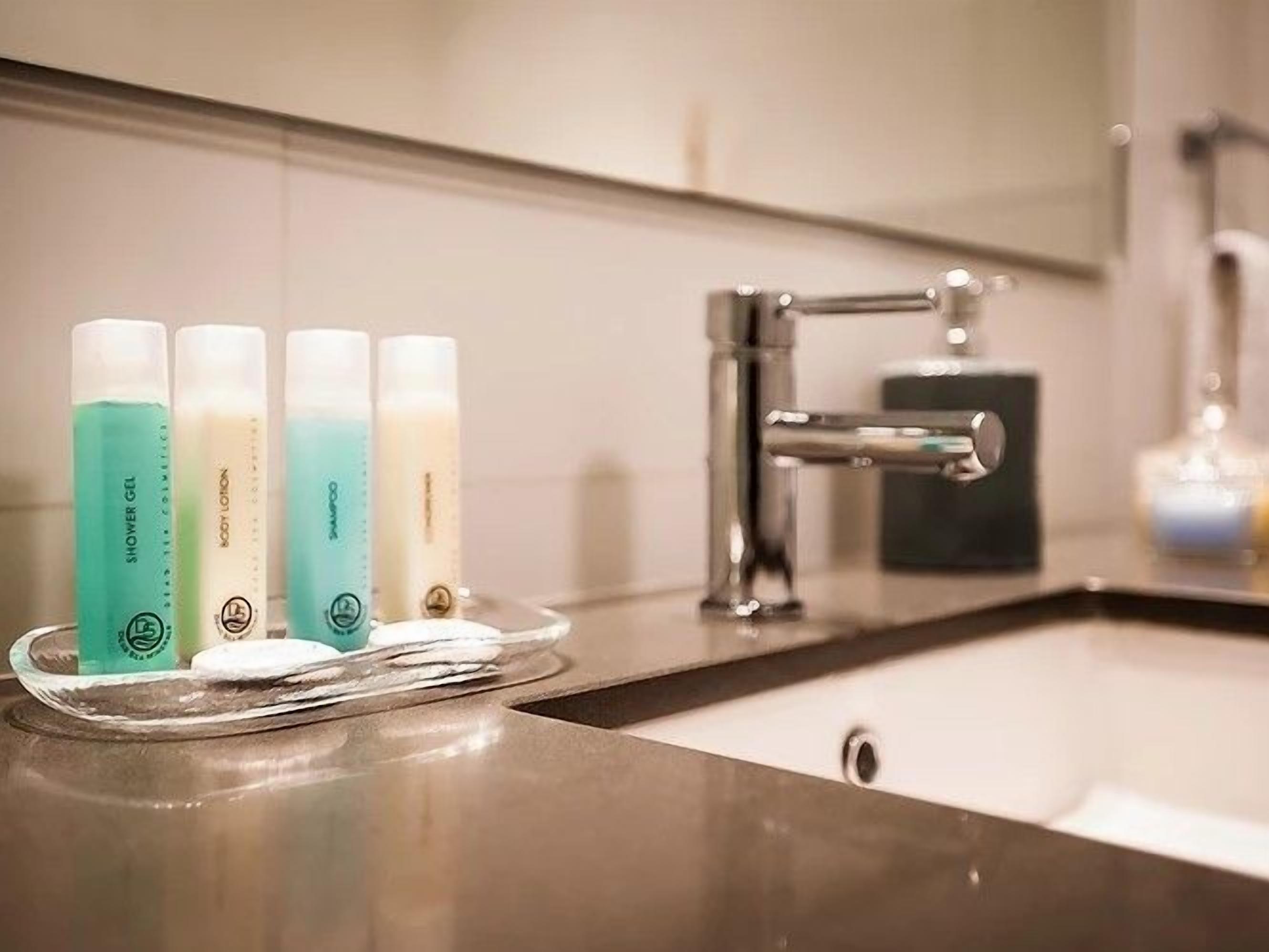 A bathroom with a sink, a mirror, and a tray holding four bottles of body lotion.