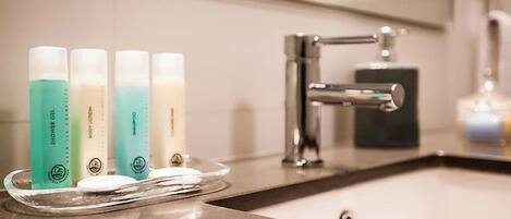 A bathroom with a sink, a mirror, and a tray holding four bottles of body lotion.